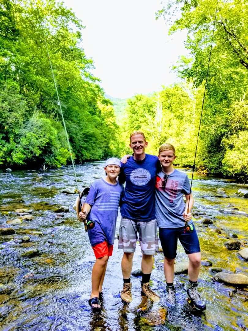 Three people standing near a lake, smiling at the camera