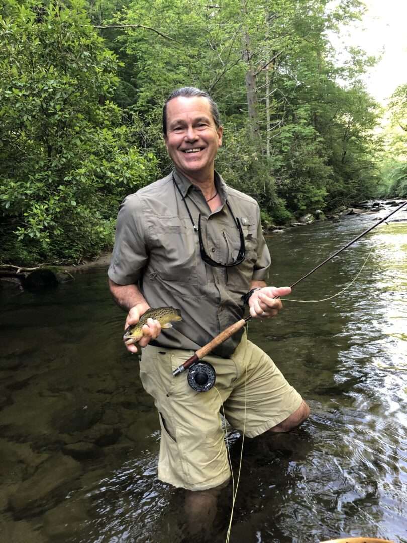 A man standing near a lake, smiling at the camera