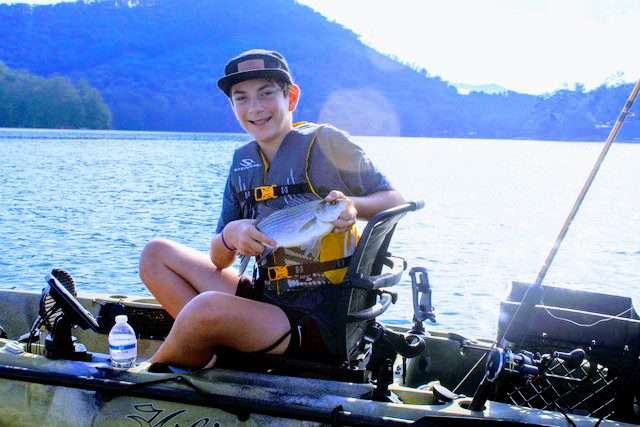 A small boy holding a fish while boating